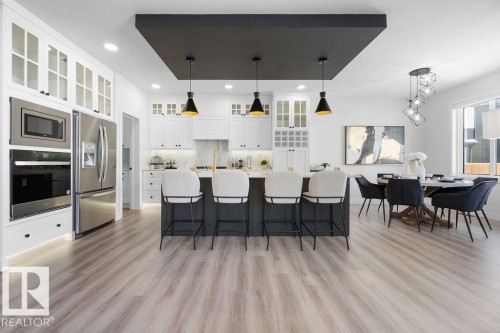 Kitchen featuring stainless steel appliances, a large island, a kitchen bar, hanging light fixtures, and glass insert cabinets - 3722 41 Avenue, Beaumont, AB - Indoor