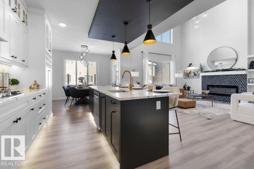 Kitchen with open floor plan, two tone cabinetry, light stone countertops, glass fronted cabinets, and a fireplace - 3722 41 Avenue, Beaumont, AB - Indoor Photo Showing Kitchen With Upgraded Kitchen