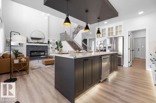 Two tone kitchen featuring open floor plan, a fireplace, pendant lighting, glass fronted cabinets, and a kitchen island with sink - 3722 41 Avenue, Beaumont, AB - Indoor Photo Showing Kitchen With Fireplace With Upgraded Kitchen
