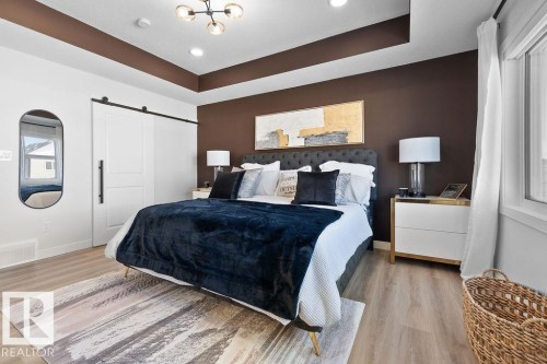 Bedroom featuring a barn door, a tray ceiling, light wood-type flooring, and recessed lighting - 3722 41 Avenue, Beaumont, AB - Indoor Photo Showing Bedroom