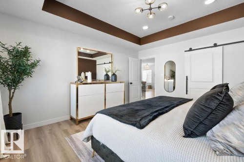Bedroom featuring a barn door, a tray ceiling, light wood-style floors, and recessed lighting - 3722 41 Avenue, Beaumont, AB - Indoor Photo Showing Bedroom