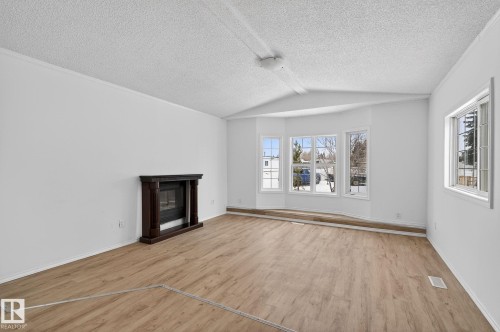 Unfurnished living room featuring a glass covered fireplace, light wood-style flooring, and a textured ceiling - 72 Evergreen Park, Edmonton, AB - Indoor Photo Showing Living Room With Fireplace