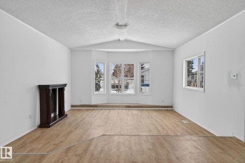 Unfurnished living room with a fireplace with raised hearth, healthy amount of natural light, light wood-style flooring, and a textured ceiling - 72 Evergreen Park, Edmonton, AB - Indoor Photo Showing Other Room