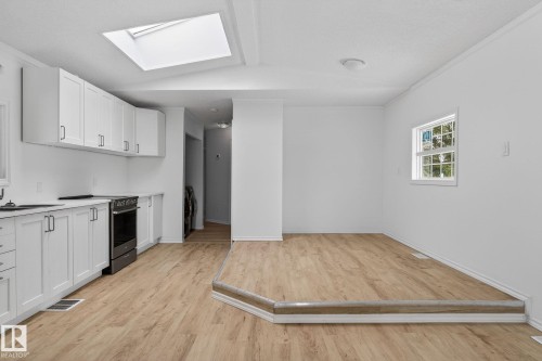 Kitchen featuring light countertops, white cabinets, a skylight, ornamental molding, and light wood-type flooring - 72 Evergreen Park, Edmonton, AB - Indoor