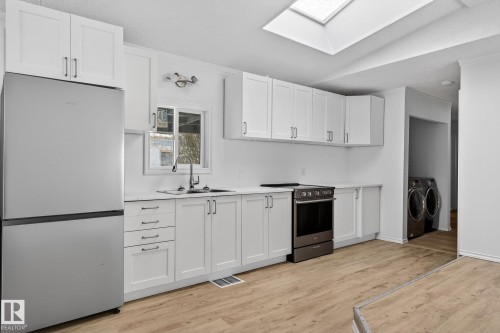 Kitchen with stainless steel appliances, white cabinets, a skylight, light wood-type flooring, and vaulted ceiling - 72 Evergreen Park, Edmonton, AB - Indoor Photo Showing Kitchen With Double Sink
