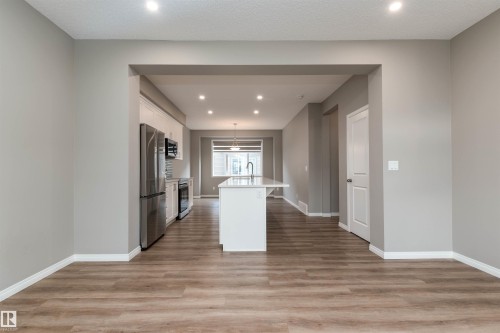 Kitchen with a center island with sink, white cabinets, recessed lighting, decorative light fixtures, and light wood-type flooring - 105 2072 Wonnacott Way, Edmonton, AB - Indoor Photo Showing Other Room
