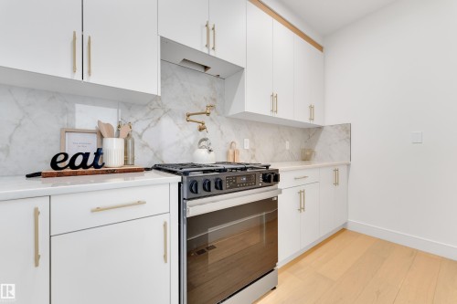 Kitchen featuring white cabinetry, stainless steel range with gas cooktop, tasteful backsplash, and light wood-style flooring - 2408 1 Ave Sw, Edmonton, AB - Indoor Photo Showing Kitchen