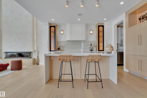 Kitchen featuring modern cabinets, an island with sink, light wood-type flooring, light stone counters, and a glass covered fireplace - 2408 1 Ave Sw, Edmonton, AB - Indoor Photo Showing Kitchen