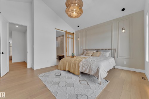Bedroom featuring light wood-style floors, lofted ceiling, connected bathroom, and a barn door - 2408 1 Ave Sw, Edmonton, AB - Indoor Photo Showing Bedroom