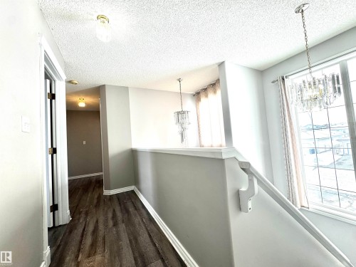Hallway featuring hanging lights, a textured ceiling, dark wood-style flooring, and an upstairs landing - 6734 162A Avenue, Edmonton, AB - Indoor Photo Showing Other Room