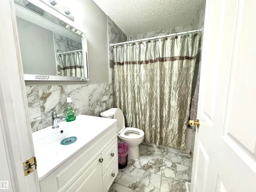 Bathroom featuring light marble finish flooring, vanity, a shower with shower curtain, a textured ceiling, and tile walls - 6734 162A Avenue, Edmonton, AB - Indoor Photo Showing Bathroom