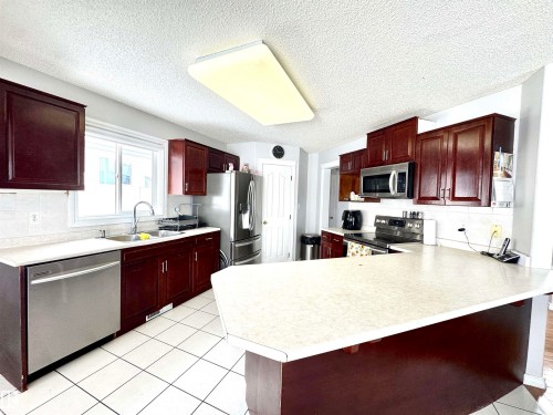 Kitchen featuring decorative backsplash, light countertops, a peninsula, bold wood finish cabinets, and a textured ceiling - 6734 162A Avenue, Edmonton, AB - Indoor Photo Showing Kitchen