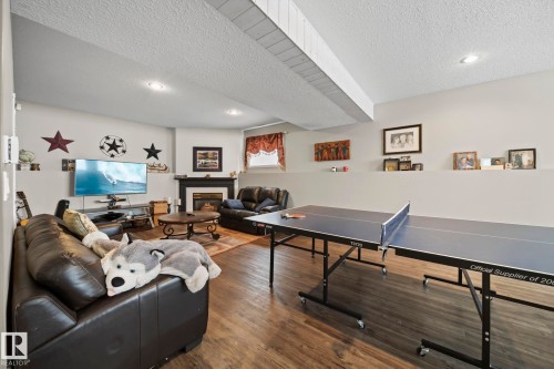 Recreation room with a glass covered fireplace, wood finished floors, recessed lighting, and a textured ceiling - 103 Adams Close, Red Deer, AB - Indoor