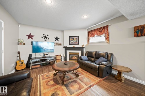 Living area featuring wood finished floors, a glass covered fireplace, and a textured ceiling - 103 Adams Close, Red Deer, AB - Indoor Photo Showing Living Room With Fireplace