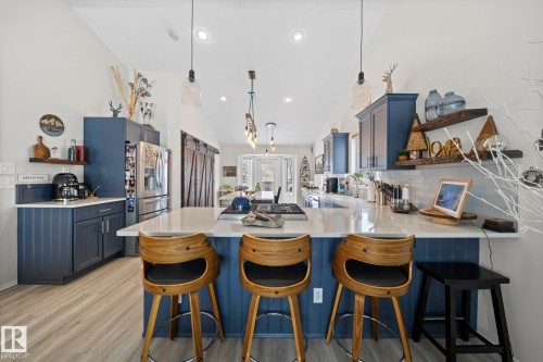 Kitchen with a breakfast bar area, open shelves, a peninsula, blue cabinets, and light stone countertops - 103 Adams Close, Red Deer, AB - Indoor Photo Showing Other Room