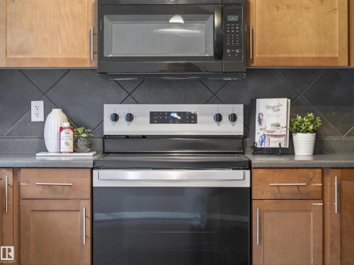 Kitchen with black microwave, electric range, tasteful backsplash, and wood finish cabinets - 125 655 Tamarack Road, Edmonton, AB - Indoor Photo Showing Kitchen