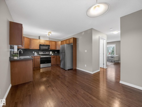 Kitchen with wood finish cabinetry, stainless steel appliances, dark countertops, dark wood-style flooring, and backsplash - 125 655 Tamarack Road, Edmonton, AB - Indoor Photo Showing Kitchen