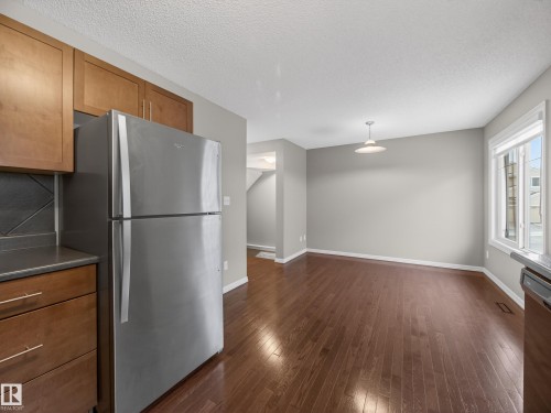 Kitchen with stainless steel appliances, wood finish cabinetry, dark wood-style floors, a textured ceiling, and dark countertops - 125 655 Tamarack Road, Edmonton, AB - Indoor Photo Showing Kitchen