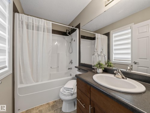 Bathroom featuring a textured ceiling, vanity, shower / tub combo with curtain, and stone finish floors - 125 655 Tamarack Road, Edmonton, AB - Indoor Photo Showing Bathroom