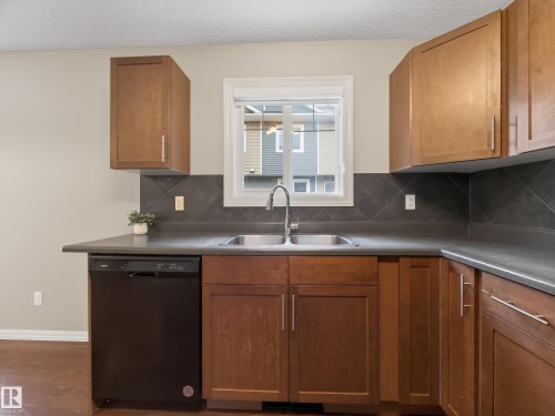 Kitchen with black dishwasher, dark countertops, wood finish cabinets, tasteful backsplash, and a textured ceiling - 125 655 Tamarack Road, Edmonton, AB - Indoor Photo Showing Kitchen With Double Sink