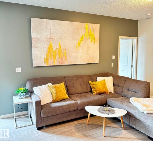 Living area featuring light wood-finish flooring, a painted accent wall, and a textured white ceiling - 437 1818 Rutherford Road, Edmonton, AB - Indoor Photo Showing Living Room