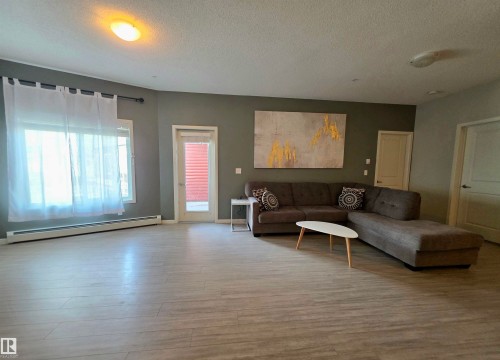Living area featuring a baseboard radiator, a textured ceiling, and wood finished floors - 437 1818 Rutherford Road, Edmonton, AB - Indoor Photo Showing Other Room