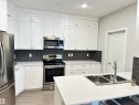 Modern kitchen featuring white shaker-style cabinetry, stainless steel appliances, dark subway tile backsplash, light-toned countertops, and wood-finish flooring - 437 1818 Rutherford Road, Edmonton, AB  - Indoor Photo Showing Kitchen With Stainless Steel Kitchen With Double Sink With Upgraded Kitchen 