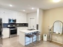 Modern kitchen featuring white shaker cabinetry, stainless steel appliances, a dark subway tile backsplash, a central island with a double sink, and light wood-finish flooring - 437 1818 Rutherford Road, Edmonton, AB  - Indoor Photo Showing Kitchen With Stainless Steel Kitchen With Double Sink 