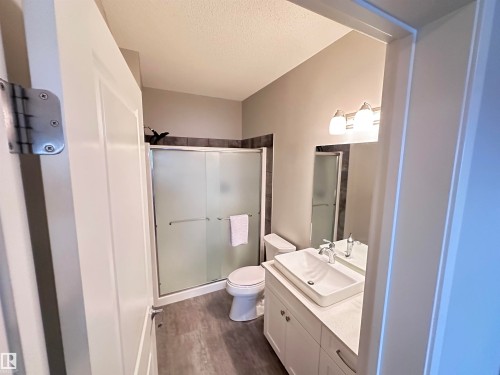 Bathroom featuring a white vanity with vessel sink, wood-finish flooring, and a frosted glass shower enclosure - 437 1818 Rutherford Road, Edmonton, AB - Indoor Photo Showing Bathroom