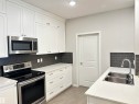 Contemporary kitchen featuring white shaker cabinetry, stainless steel appliances, white countertops, and a dark subway tile backsplash - 437 1818 Rutherford Road, Edmonton, AB  - Indoor Photo Showing Kitchen With Double Sink 