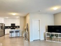 Open-concept living area featuring light wood-finish flooring, white flat-panel cabinetry, stainless steel appliances, a dark subway tile backsplash, and a kitchen island with a sink - 437 1818 Rutherford Road, Edmonton, AB  - Indoor Photo Showing Kitchen 