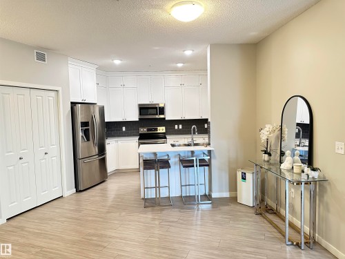 Kitchen featuring white cabinetry, stainless steel appliances, a dark subway tile backsplash, and a central island with bar seating - 437 1818 Rutherford Road, Edmonton, AB - Indoor Photo Showing Kitchen With Stainless Steel Kitchen
