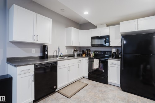 Kitchen with black appliances, white cabinetry, dark countertops, stone finish floors, and recessed lighting - 326 West Haven Drive, Leduc, AB - Indoor Photo Showing Kitchen With Double Sink
