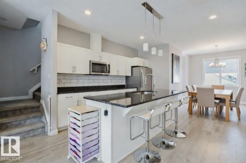 Kitchen featuring light wood-type flooring, a kitchen island with sink, a kitchen bar, dark stone countertops, and white cabinets - 326 West Haven Drive, Leduc, AB - Indoor Photo Showing Kitchen With Upgraded Kitchen