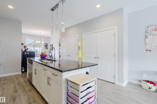 Kitchen with white cabinetry, light wood-style floors, dark stone counters, a center island with sink, and hanging lights - 326 West Haven Drive, Leduc, AB - Indoor
