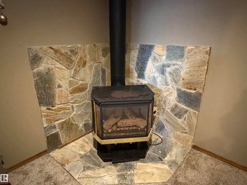 Detailed view of a wood stove and carpet floors - 2008 4Th Ave, Cold Lake, AB - Indoor With Fireplace