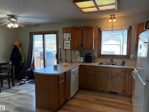Kitchen with wood finish cabinets, a peninsula, freestanding refrigerator, light countertops, and a textured ceiling - 2008 4Th Ave, Cold Lake, AB - Indoor Photo Showing Kitchen With Double Sink