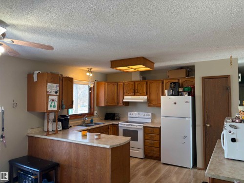 Kitchen featuring wood finish cabinets, white appliances, light countertops, a peninsula, and light wood-type flooring - 2008 4Th Ave, Cold Lake, AB - Indoor Photo Showing Kitchen With Double Sink