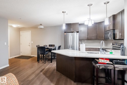 Kitchen featuring dark wood finish cabinets, a peninsula, stainless steel appliances, light stone countertops, and dark wood-type flooring - 207 2203 44 Avenue, Edmonton, AB - Indoor Photo Showing Kitchen With Stainless Steel Kitchen With Upgraded Kitchen