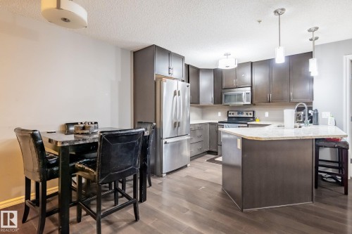 Kitchen with a breakfast bar, stainless steel appliances, a peninsula, dark wood-style floors, and a textured ceiling - 207 2203 44 Avenue, Edmonton, AB - Indoor Photo Showing Kitchen With Stainless Steel Kitchen With Upgraded Kitchen