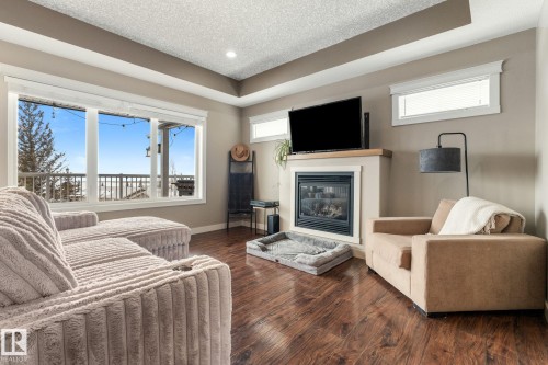 Living area with a glass covered fireplace, dark wood-type flooring, a textured ceiling, recessed lighting, and a tray ceiling - 523 55101 Ste. Anne Trail, Rural Lac Ste. Anne County, AB - Indoor Photo Showing Living Room With Fireplace