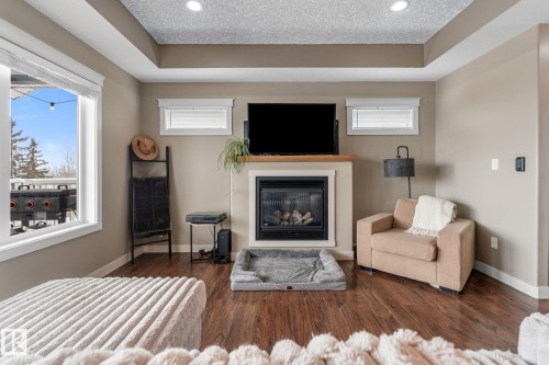 Bedroom featuring a glass covered fireplace, dark wood-style flooring, a textured ceiling, a raised ceiling, and recessed lighting - 523 55101 Ste. Anne Trail, Rural Lac Ste. Anne County, AB - Indoor Photo Showing Other Room With Fireplace