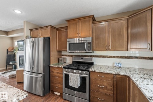 Kitchen with stainless steel appliances, dark wood-style floors, light stone countertops, wood finish cabinetry, and a textured ceiling - 523 55101 Ste. Anne Trail, Rural Lac Ste. Anne County, AB - Indoor Photo Showing Kitchen
