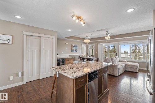 Kitchen featuring open floor plan, a kitchen island, dark wood-type flooring, a kitchen breakfast bar, and light stone countertops - 523 55101 Ste. Anne Trail, Rural Lac Ste. Anne County, AB - Indoor Photo Showing Kitchen With Upgraded Kitchen