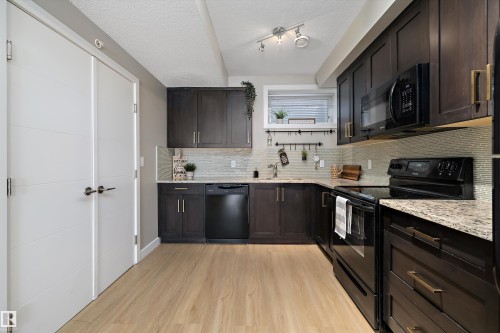 Kitchen with black appliances, dark wood finish cabinets, light wood-style flooring, a textured ceiling, and light stone countertops - 94 2560 Pegasus Boulevard, Edmonton, AB - Indoor Photo Showing Kitchen With Upgraded Kitchen