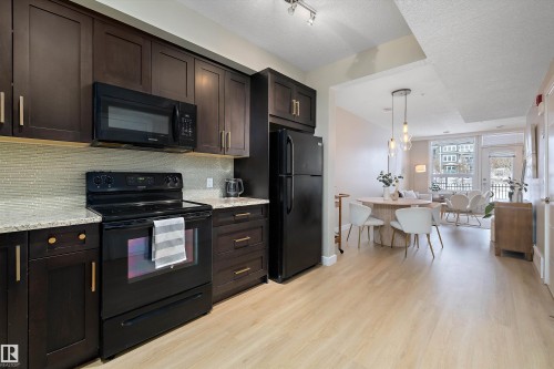 Kitchen featuring black appliances, dark wood finish cabinetry, light wood-type flooring, and a textured ceiling - 94 2560 Pegasus Boulevard, Edmonton, AB - Indoor Photo Showing Kitchen