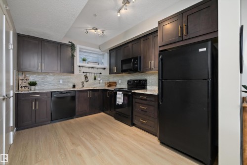 Kitchen featuring black appliances, dark wood finish cabinetry, light wood-style flooring, tasteful backsplash, and a textured ceiling - 94 2560 Pegasus Boulevard, Edmonton, AB - Indoor Photo Showing Kitchen