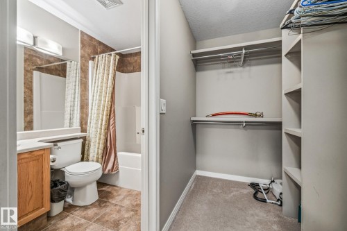 Bathroom featuring vanity, light carpet, a spacious closet, shower / bath combination with curtain, and a textured ceiling - 221 5005 165 Avenue, Edmonton, AB - Indoor Photo Showing Bathroom