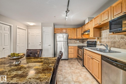 Kitchen featuring stainless steel appliances, tasteful backsplash, light countertops, and wood finish cabinetry - 221 5005 165 Avenue, Edmonton, AB - Indoor Photo Showing Kitchen With Double Sink
