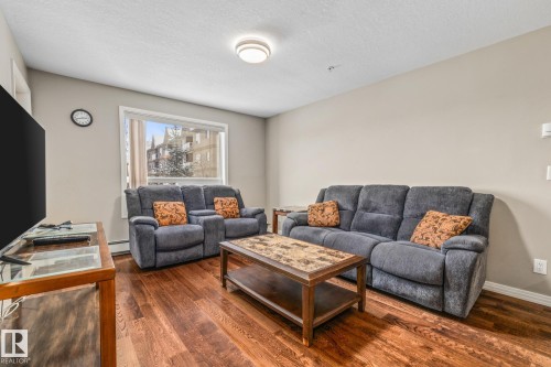 Living area with dark wood-style flooring, a textured ceiling, and a baseboard heating unit - 221 5005 165 Avenue, Edmonton, AB - Indoor Photo Showing Living Room